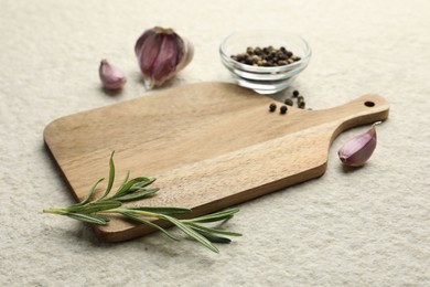 Photo of Cutting board, garlic, pepper and rosemary on white textured table. Space for text