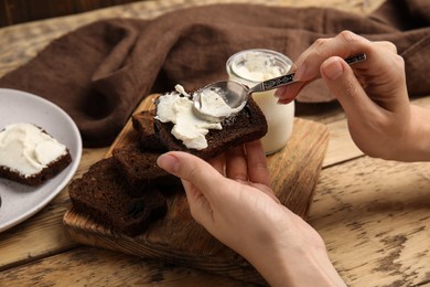 Photo of Woman spreading cream cheese onto bread at wooden table, closeup