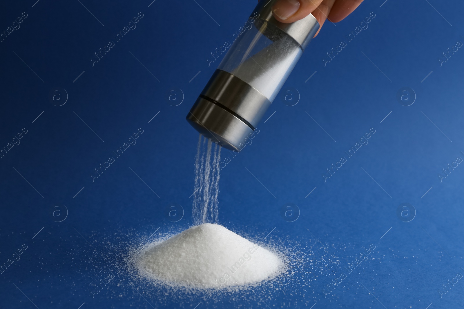 Photo of Woman pouring salt from shaker on blue background, closeup