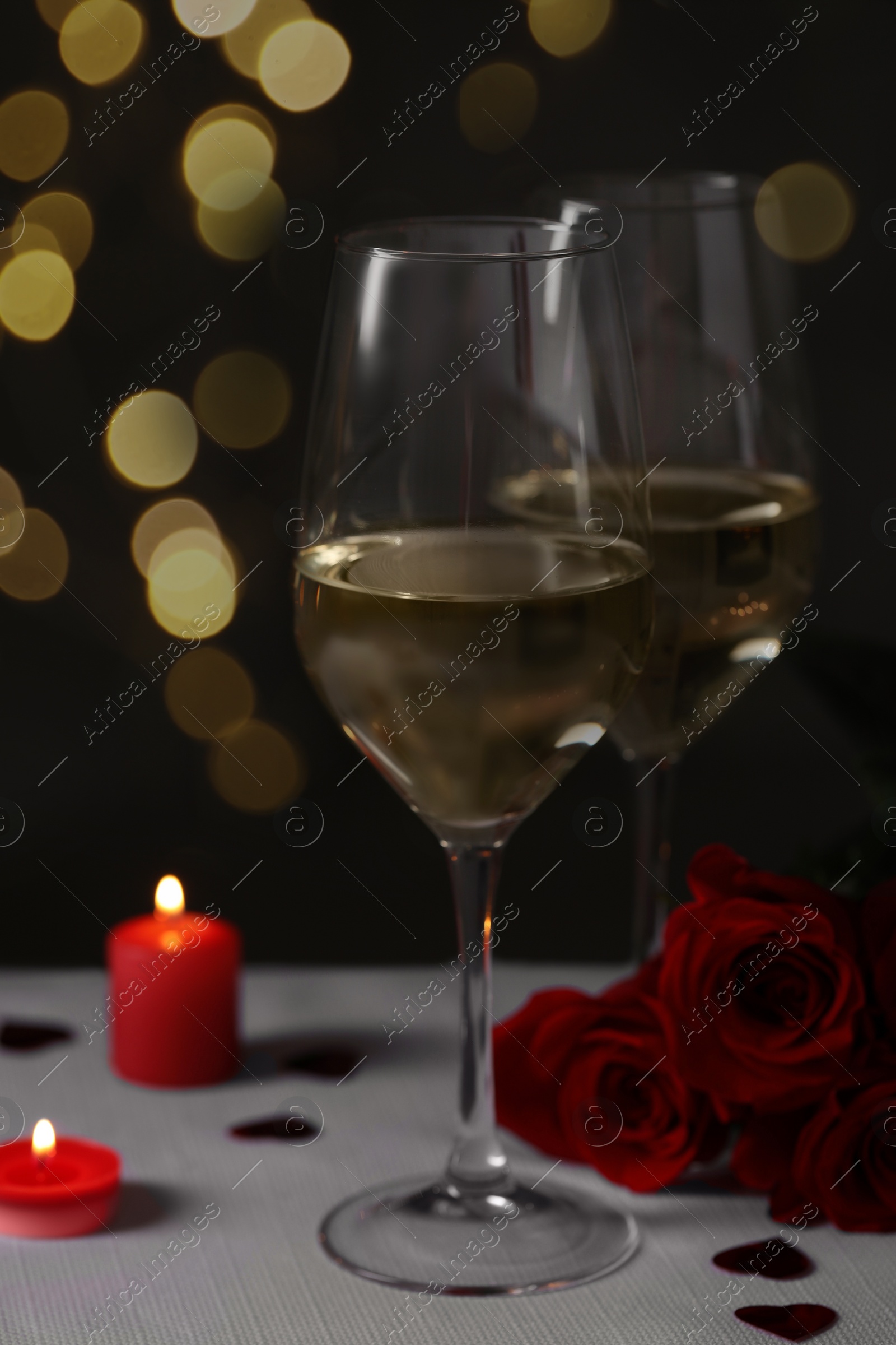 Photo of Glasses of white wine, rose flowers and burning candles on grey table against blurred background. Romantic atmosphere
