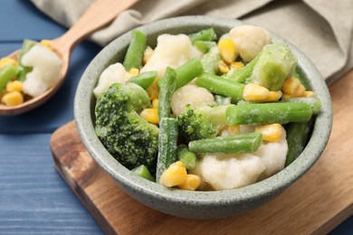 Mix of different frozen vegetables in bowl on blue wooden table, closeup