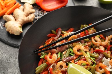 Photo of Shrimp stir fry with vegetables and chopsticks in wok on grey table, closeup