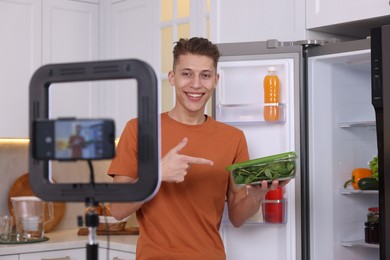 Photo of Smiling food blogger explaining something while recording video in kitchen