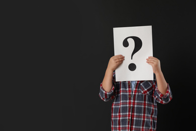 Photo of Child holding sheet of paper with question mark on black background. Space for text