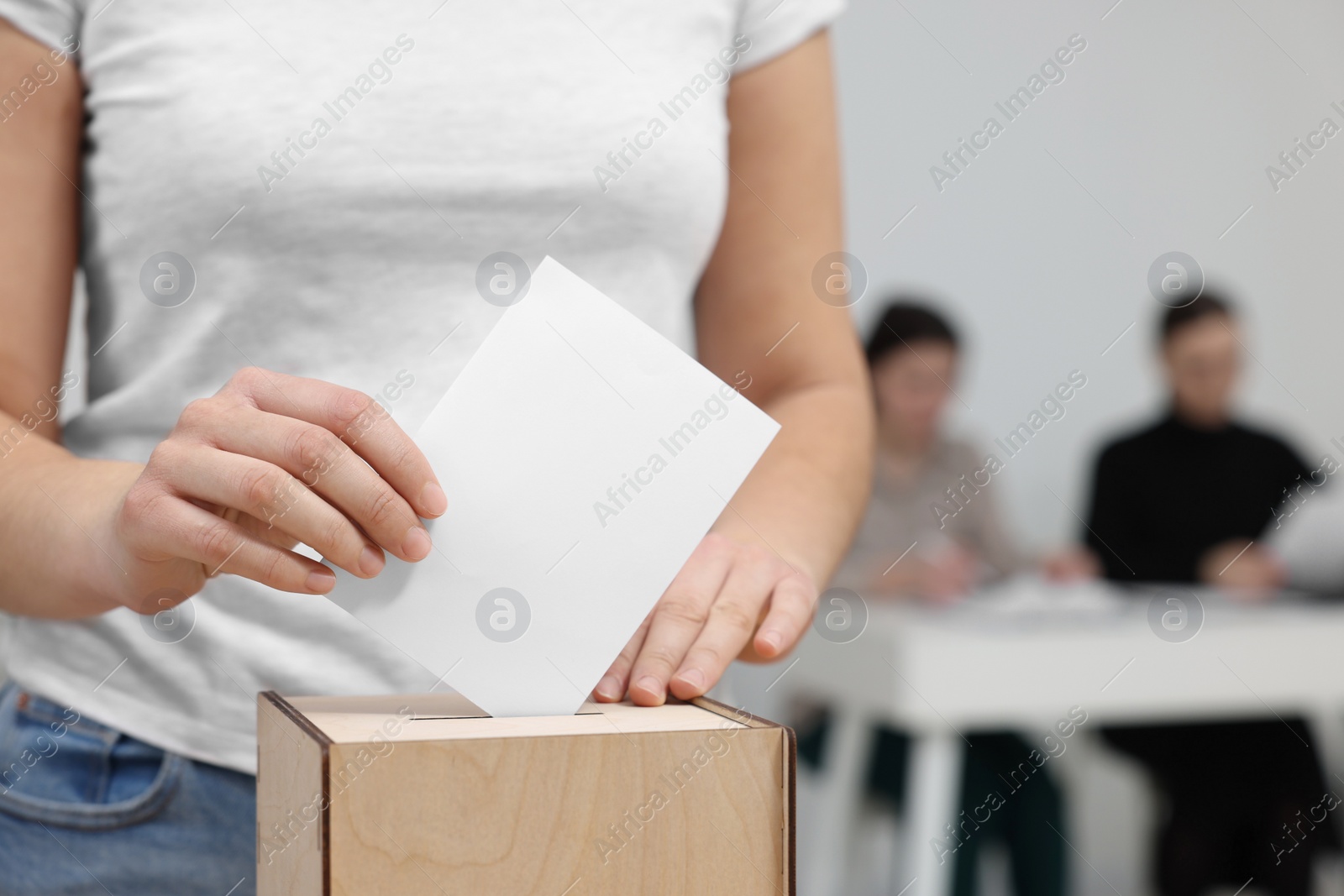 Photo of Woman putting her vote into ballot box on blurred background, closeup