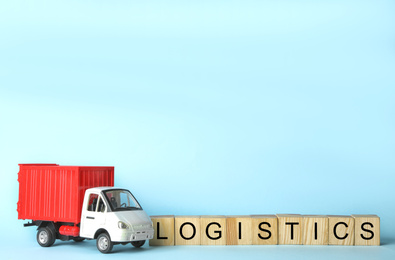 Photo of Toy truck and cubes with word LOGISTICS on light blue background, space for text. Wholesale concept