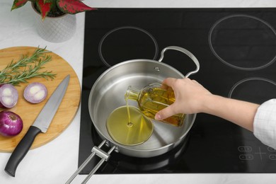 Woman pouring aromatic cooking oil from bottle into frying pan in kitchen, closeup