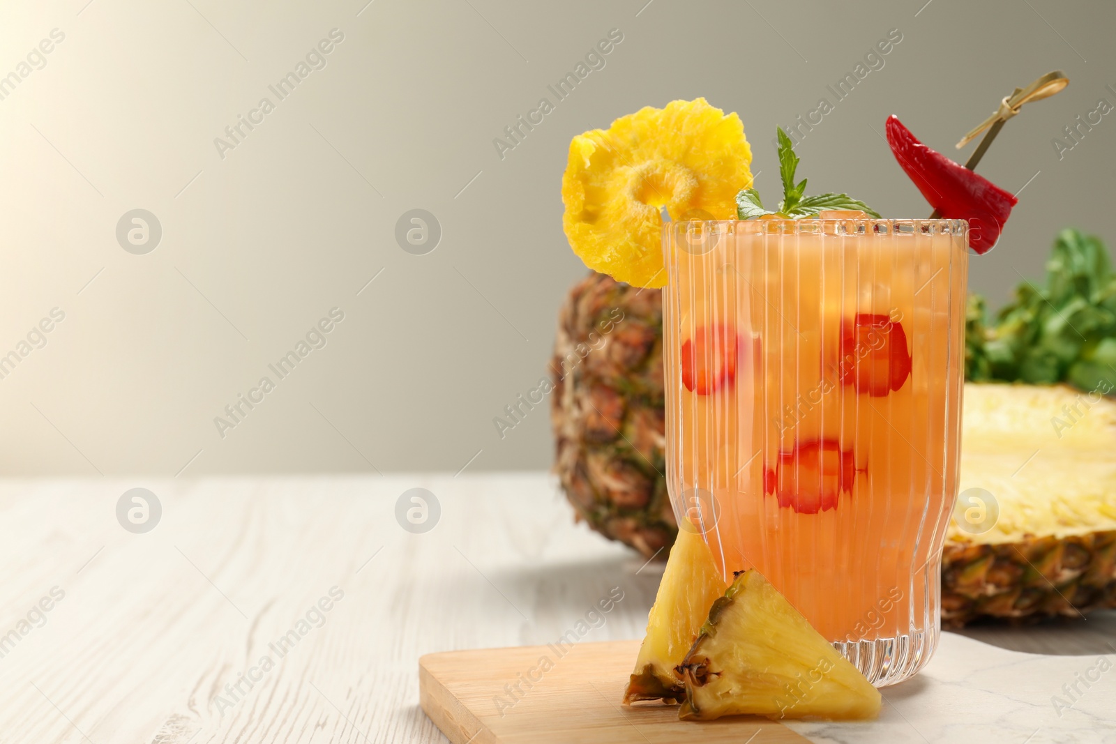 Photo of Glass of spicy pineapple cocktail with chili pepper on white table, space for text