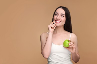 Photo of Beautiful young woman with vitamin pill and apple on beige background