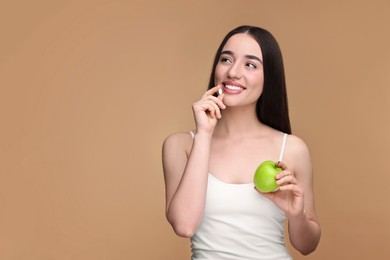 Beautiful young woman with vitamin pill and apple on beige background