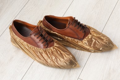 Photo of Men`s shoes in shoe covers on light wooden floor