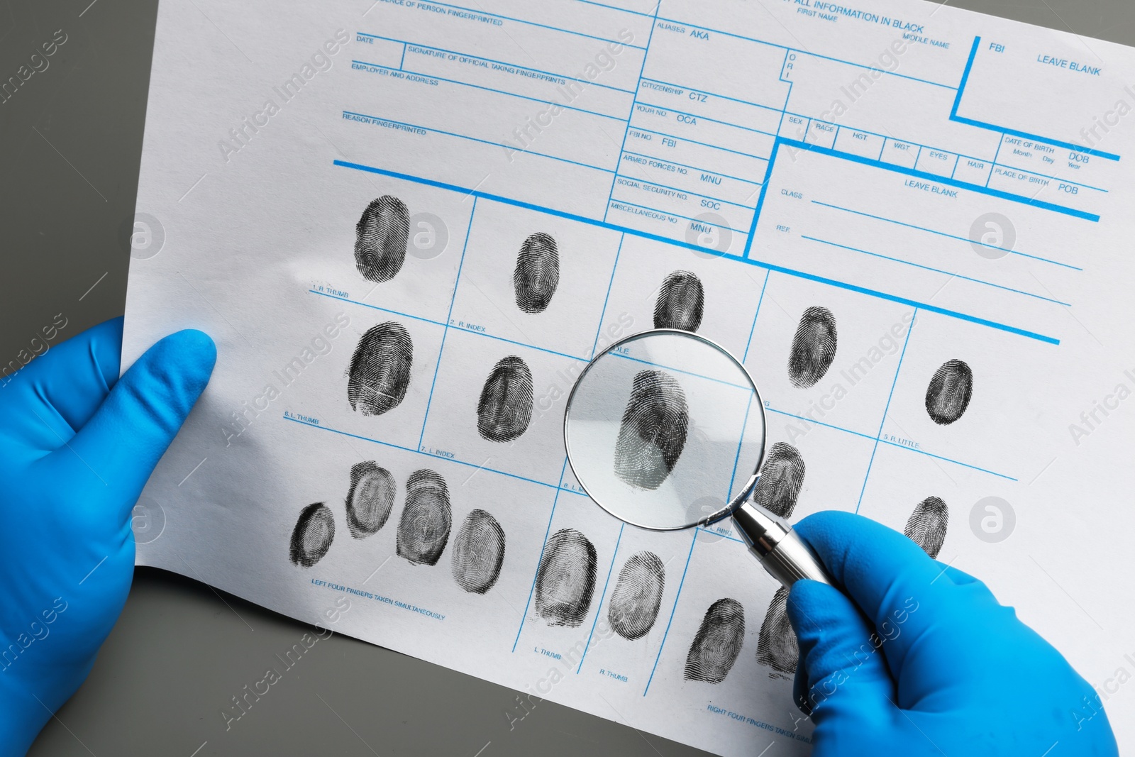 Photo of Criminalist studying fingerprints with magnifying glass at table, closeup