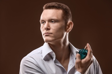 Photo of Handsome man in shirt using perfume on dark background