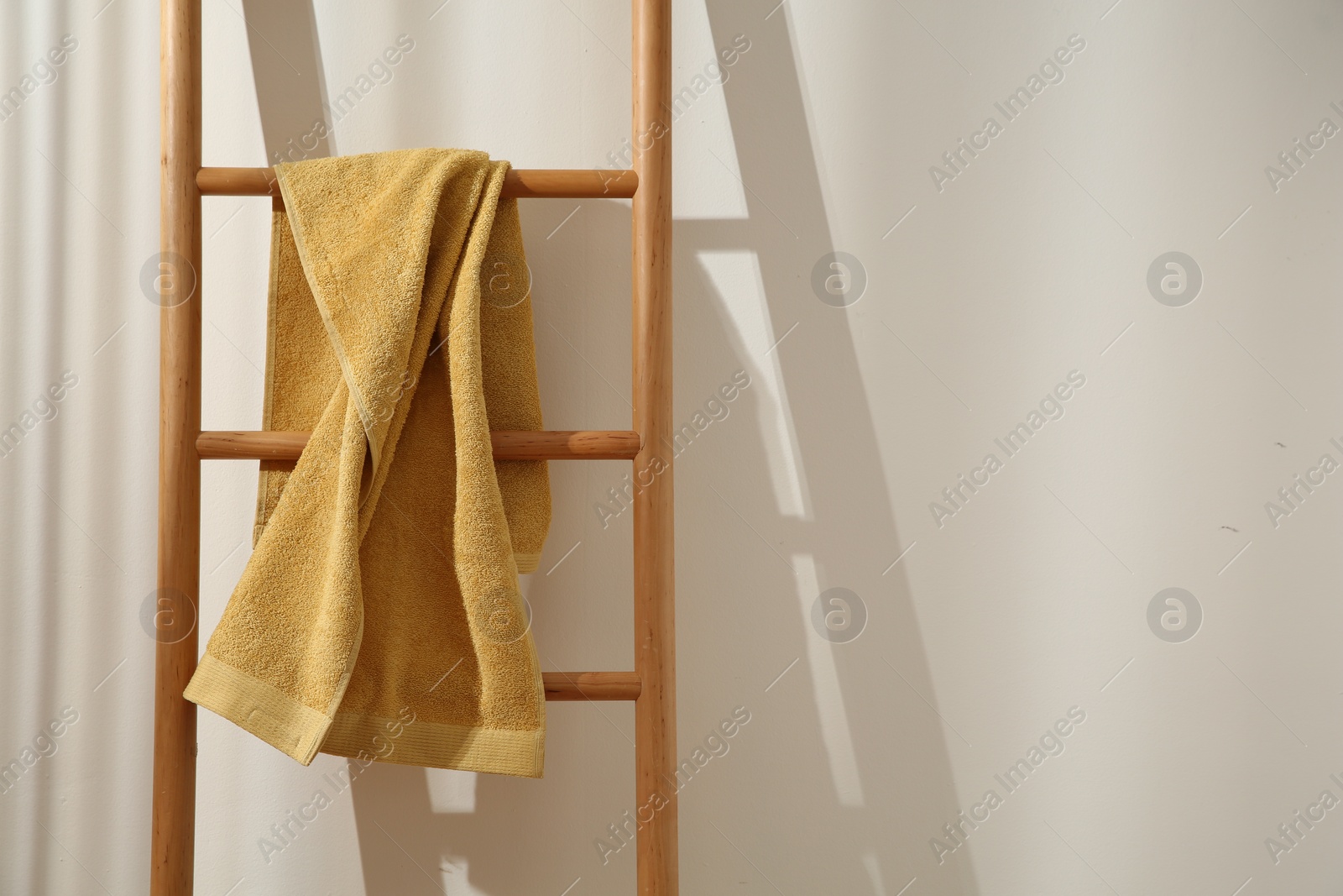 Photo of Yellow towel hanging on wooden ladder indoors. Space for text