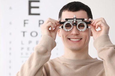 Photo of Young man with trial frame against vision test chart