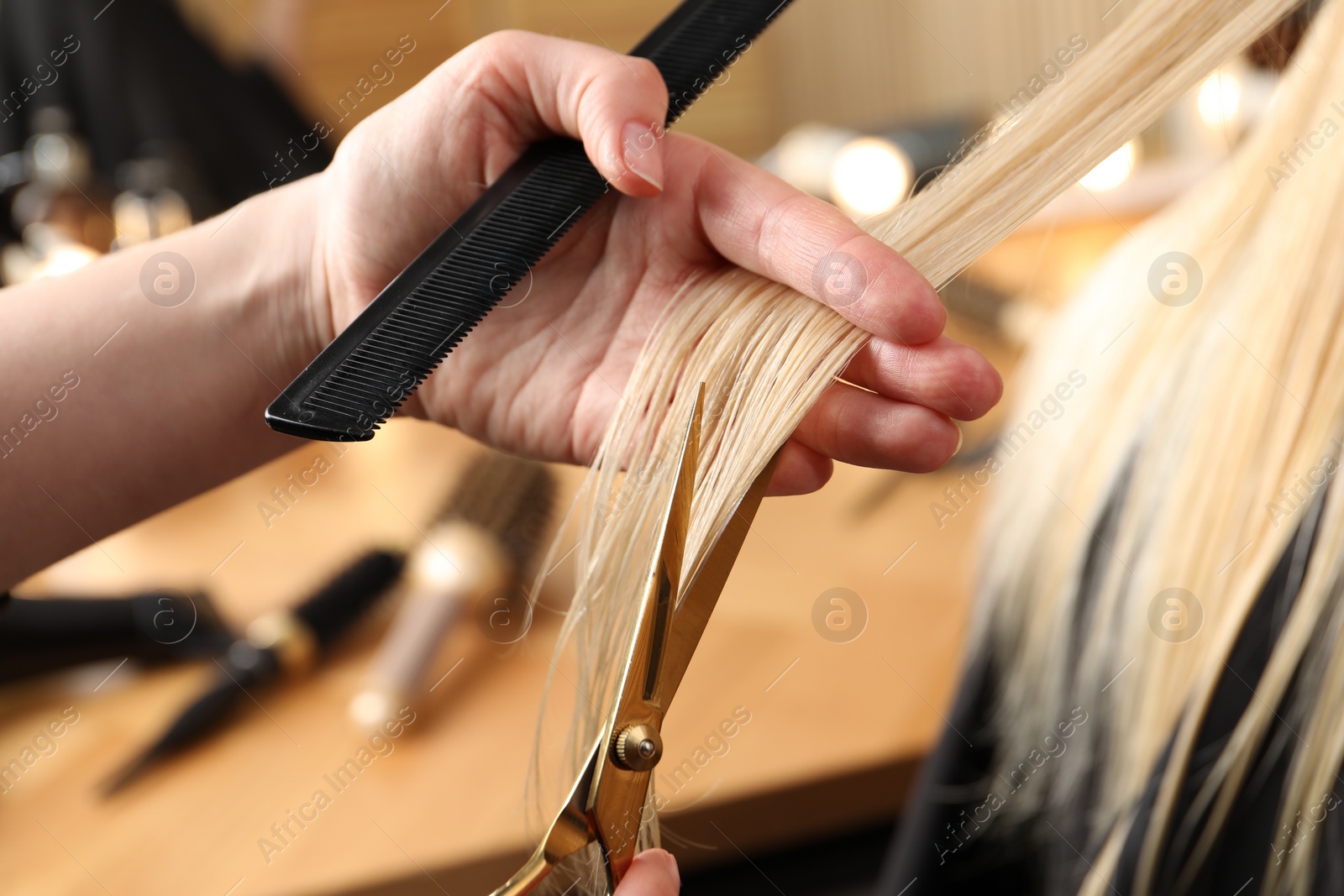 Photo of Hairdresser cutting client's hair with scissors in salon, closeup