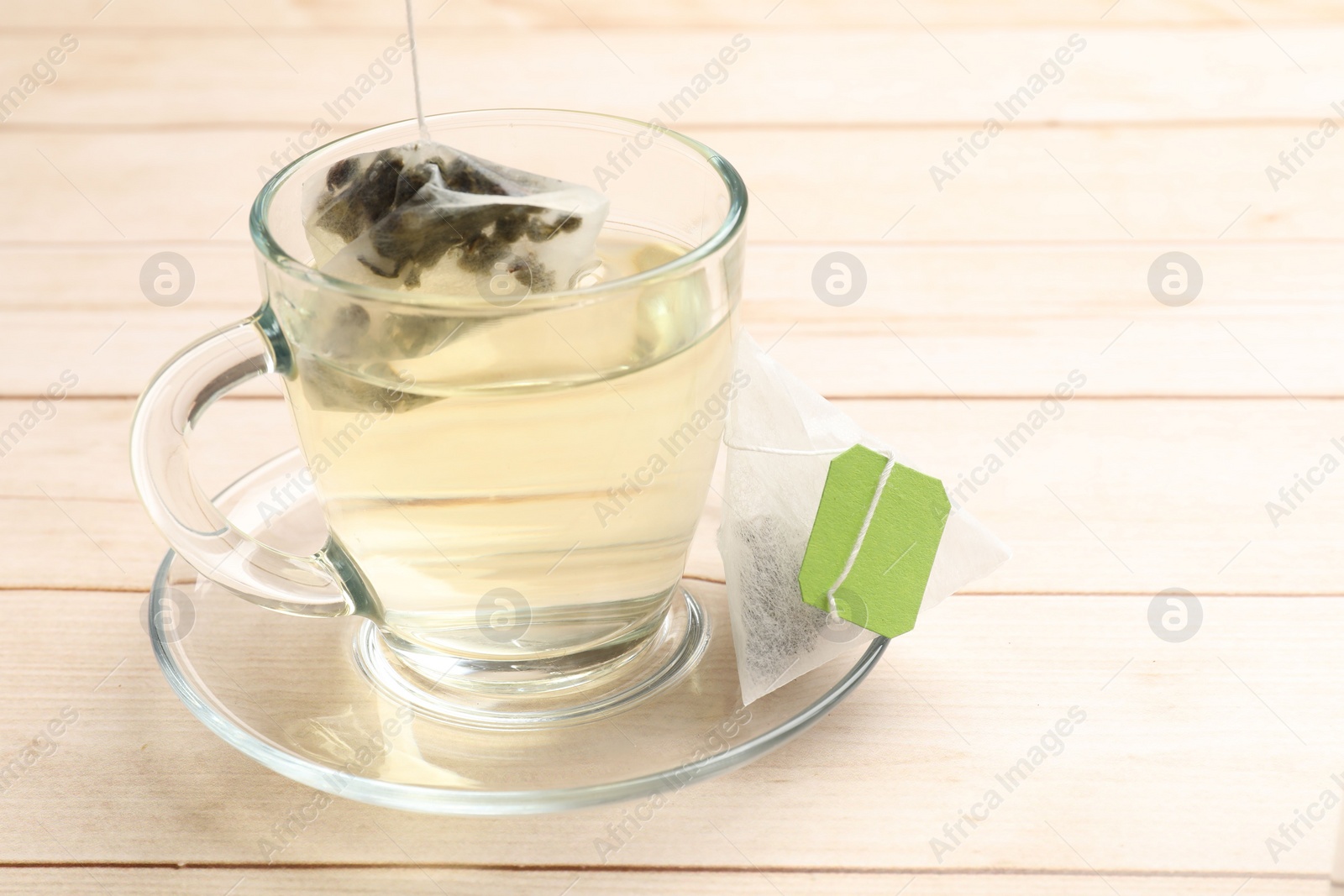 Photo of Putting tea bag in glass cup on light wooden table, closeup. Space for text