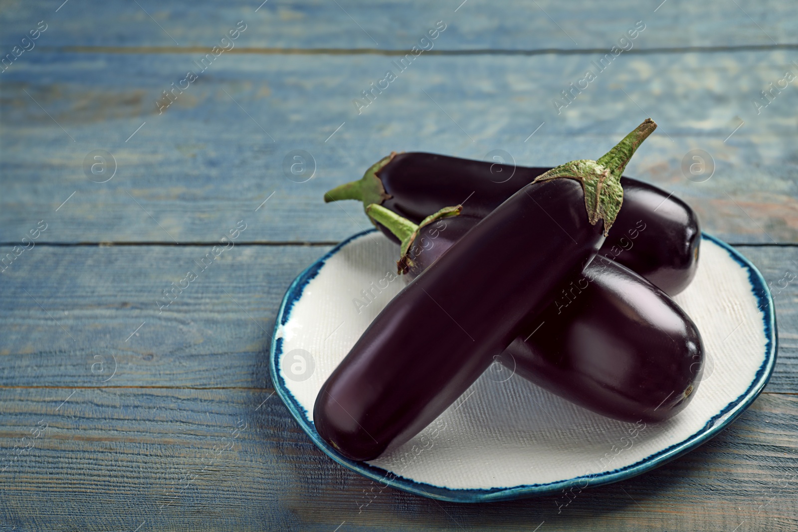 Photo of Plate with raw ripe eggplants on wooden background