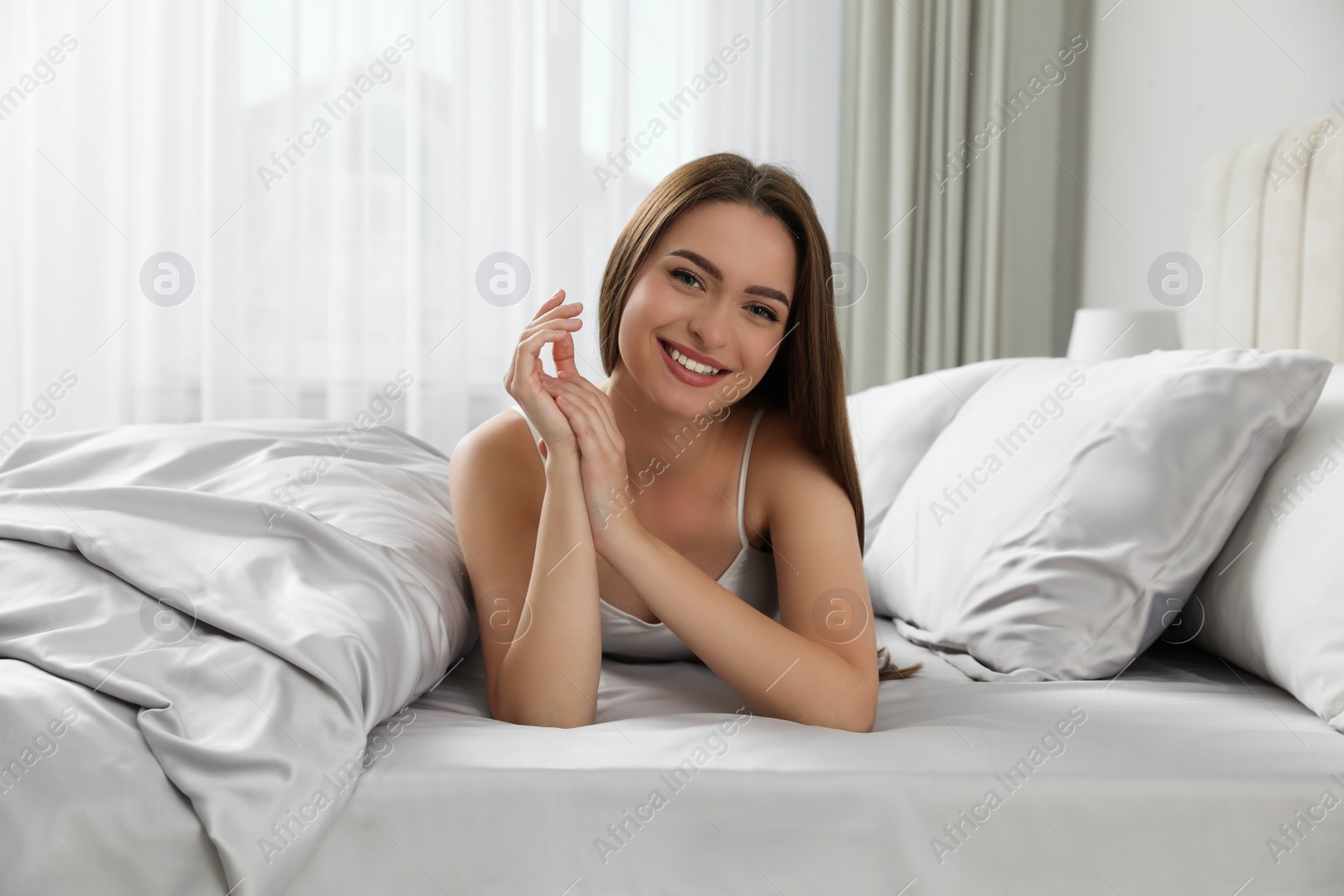 Photo of Young woman lying on comfortable bed with silky linens