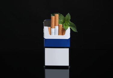 Photo of Pack of menthol cigarettes and mint on black background
