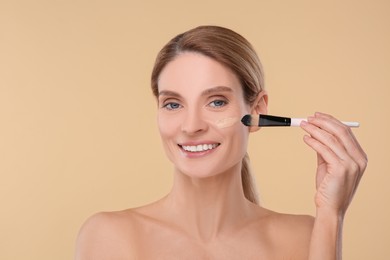 Woman applying foundation on face with brush against beige background