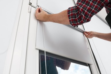 Worker installing roller window blind indoors, closeup