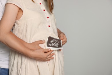 Photo of Man hugging his pregnant wife with ultrasound scan on light background, closeup. Space for text