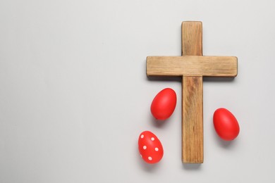 Wooden cross and painted Easter eggs on light grey background, flat lay. Space for text