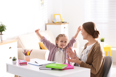 Photo of Mother and daughter doing homework together at table indoors