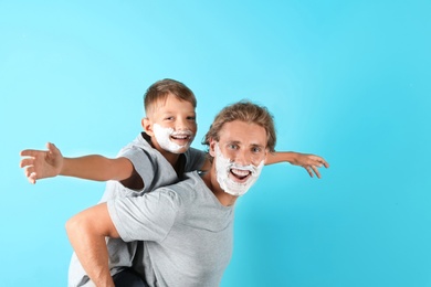 Father and son playing with shaving foam on faces against color background, space for text