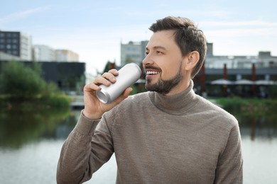 Photo of Handsome man drinking from tin can near river outdoors