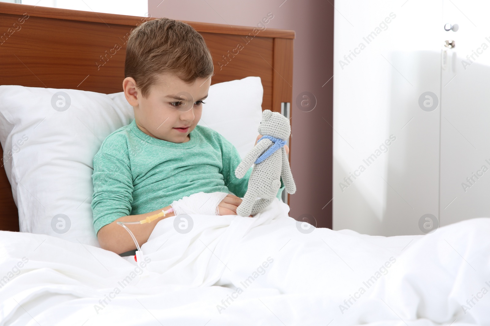 Photo of Little child with intravenous drip and toy in hospital bed