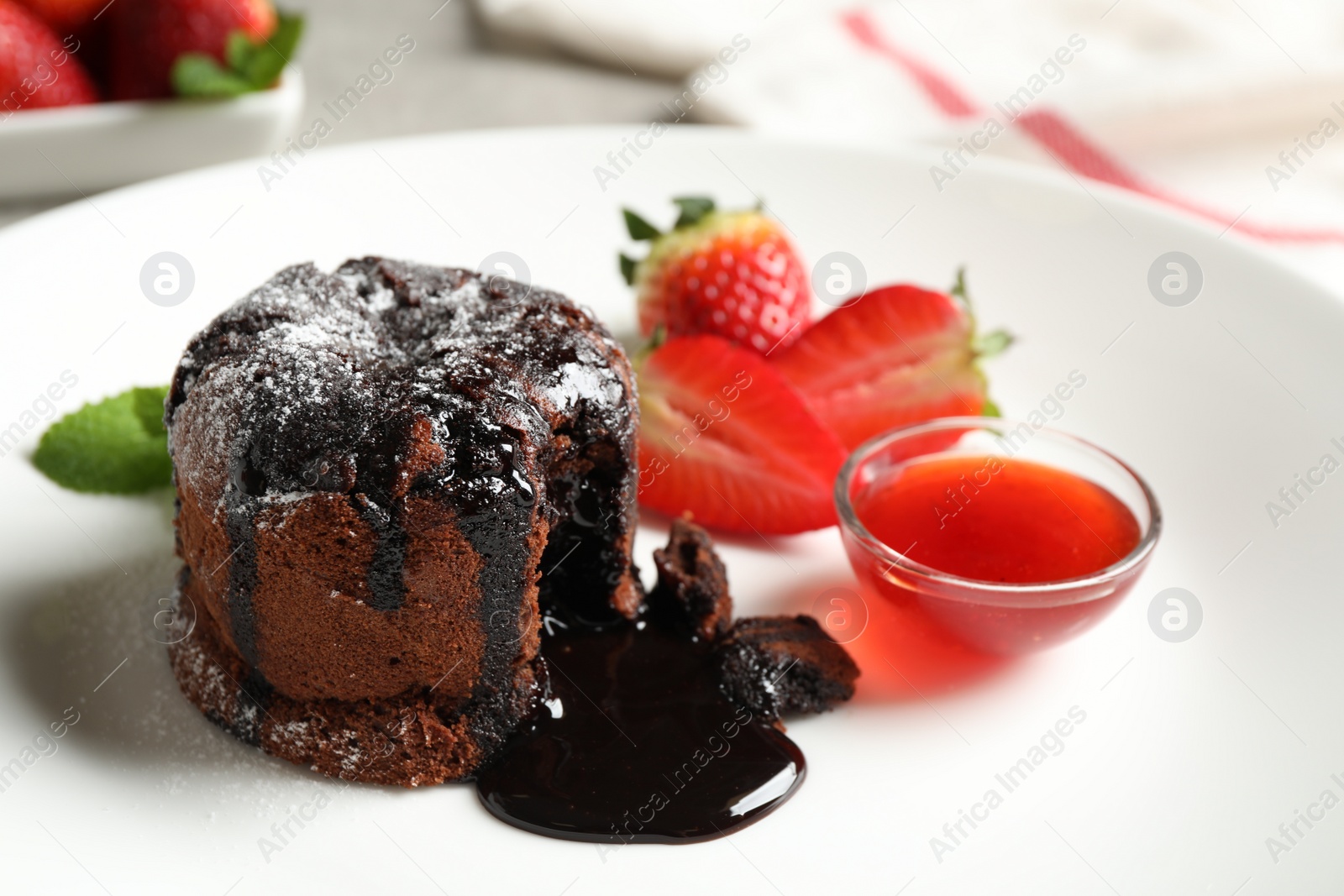 Photo of Delicious warm chocolate lava cake with mint and strawberries on plate, closeup