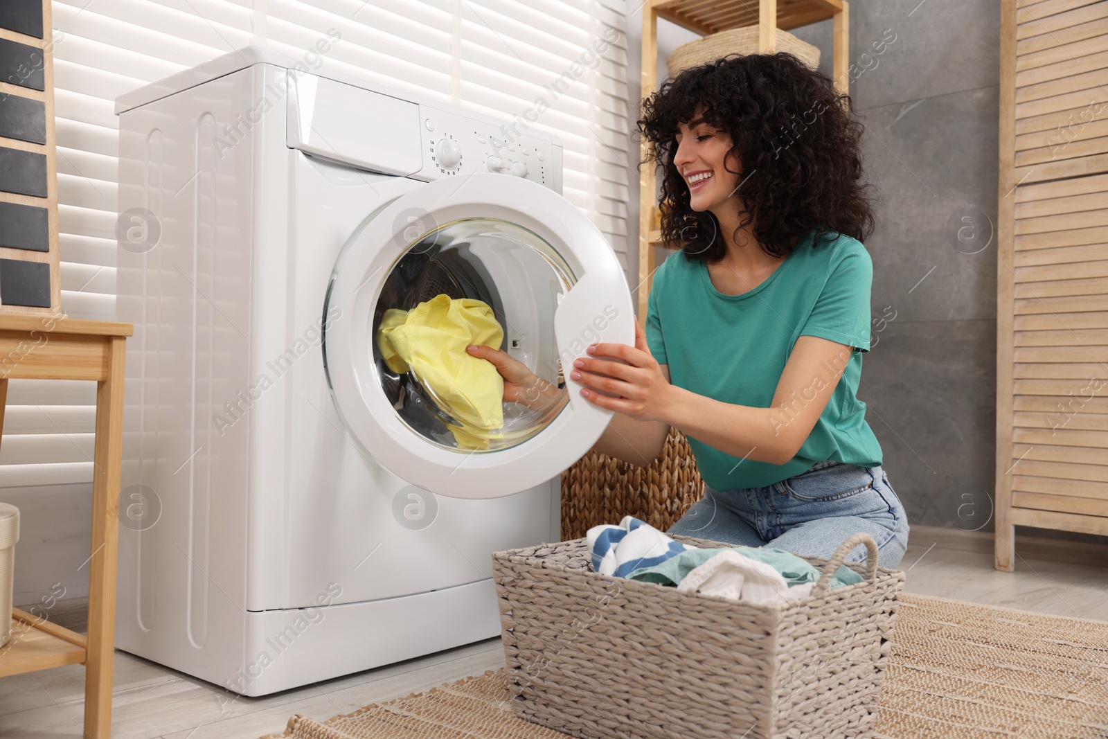 Photo of Happy woman putting laundry into washing machine indoors