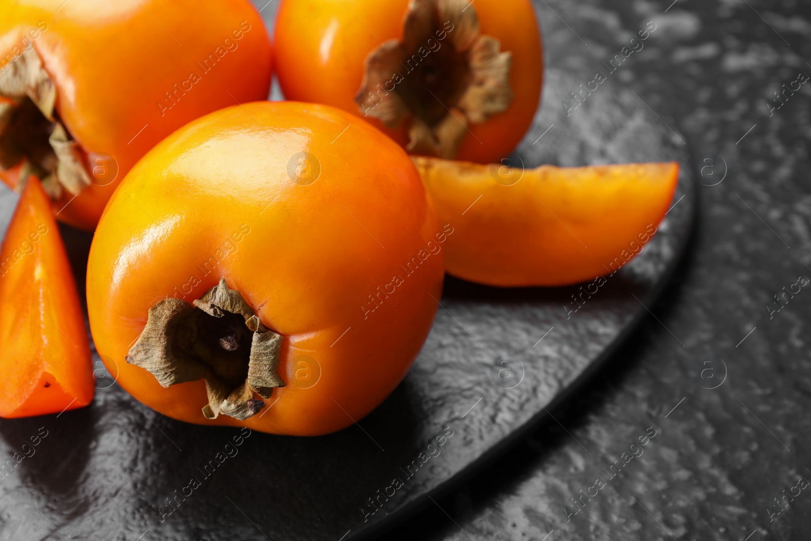 Photo of Delicious ripe persimmons on dark textured table, closeup