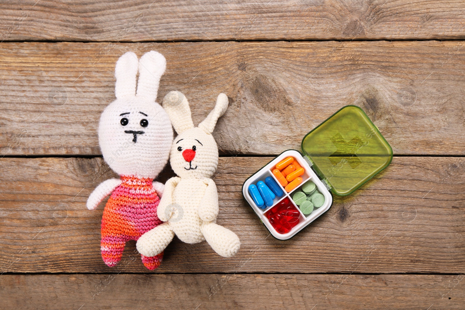 Photo of Toy bunnies and pills on wooden background, flat lay