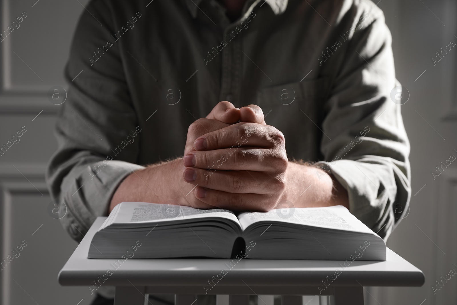 Photo of Religion. Christian man praying over Bible indoors, closeup