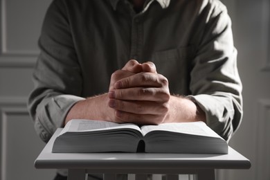 Photo of Religion. Christian man praying over Bible indoors, closeup