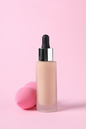 Photo of Bottle of skin foundation and sponge on pink background. Makeup product