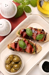 Photo of Delicious bruschettas with balsamic vinegar and toppings served with olives on white wooden table, flat lay