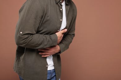 Man suffering from stomach pain on light brown background, closeup and space for text