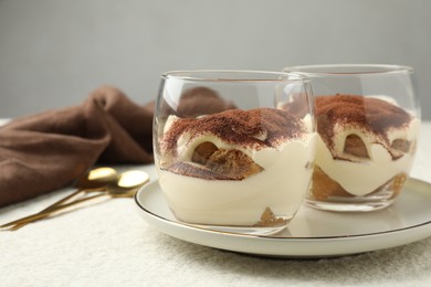 Delicious tiramisu in glasses and spoons on white table, closeup. Space for text