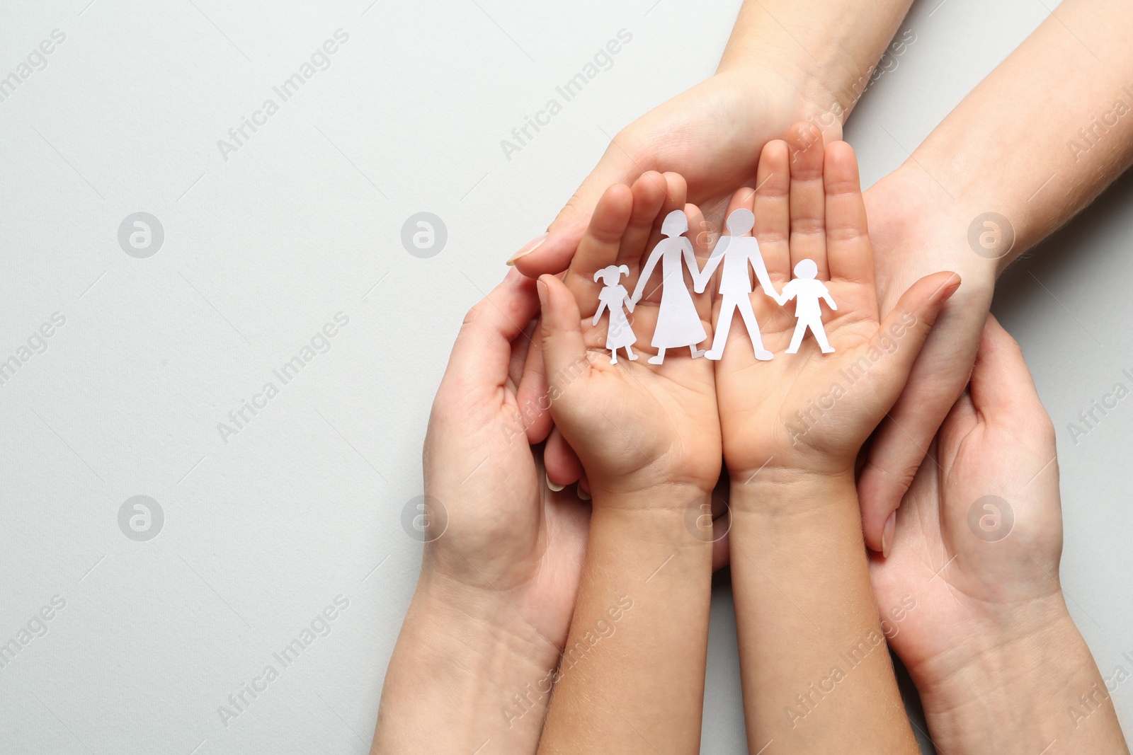 Photo of Parents and child holding paper cutout of family on light background, top view. Space for text