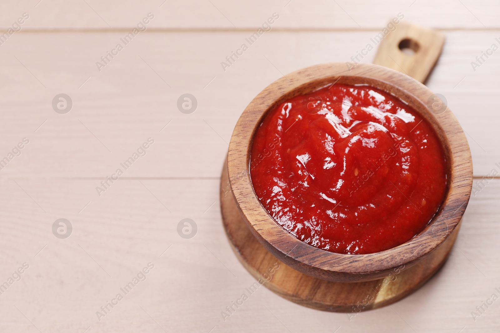 Photo of Delicious ketchup in bowl on light wooden table, closeup with space for text. Tomato sauce