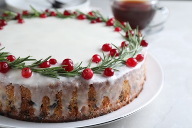Traditional Christmas cake decorated with rosemary and cranberries on light table, closeup