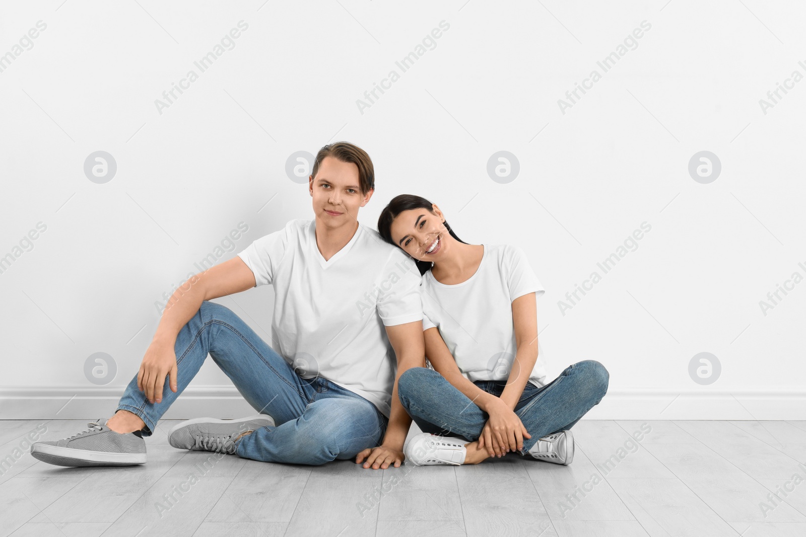 Photo of Young couple in stylish jeans sitting near white wall