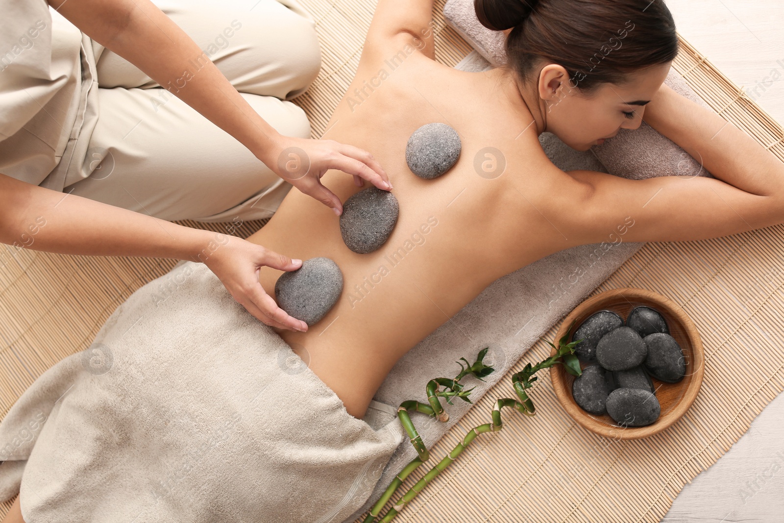 Photo of Beautiful young woman getting hot stone massage in spa salon, top view