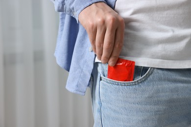 Man pulling condom out of pocket indoors, closeup. Space for text