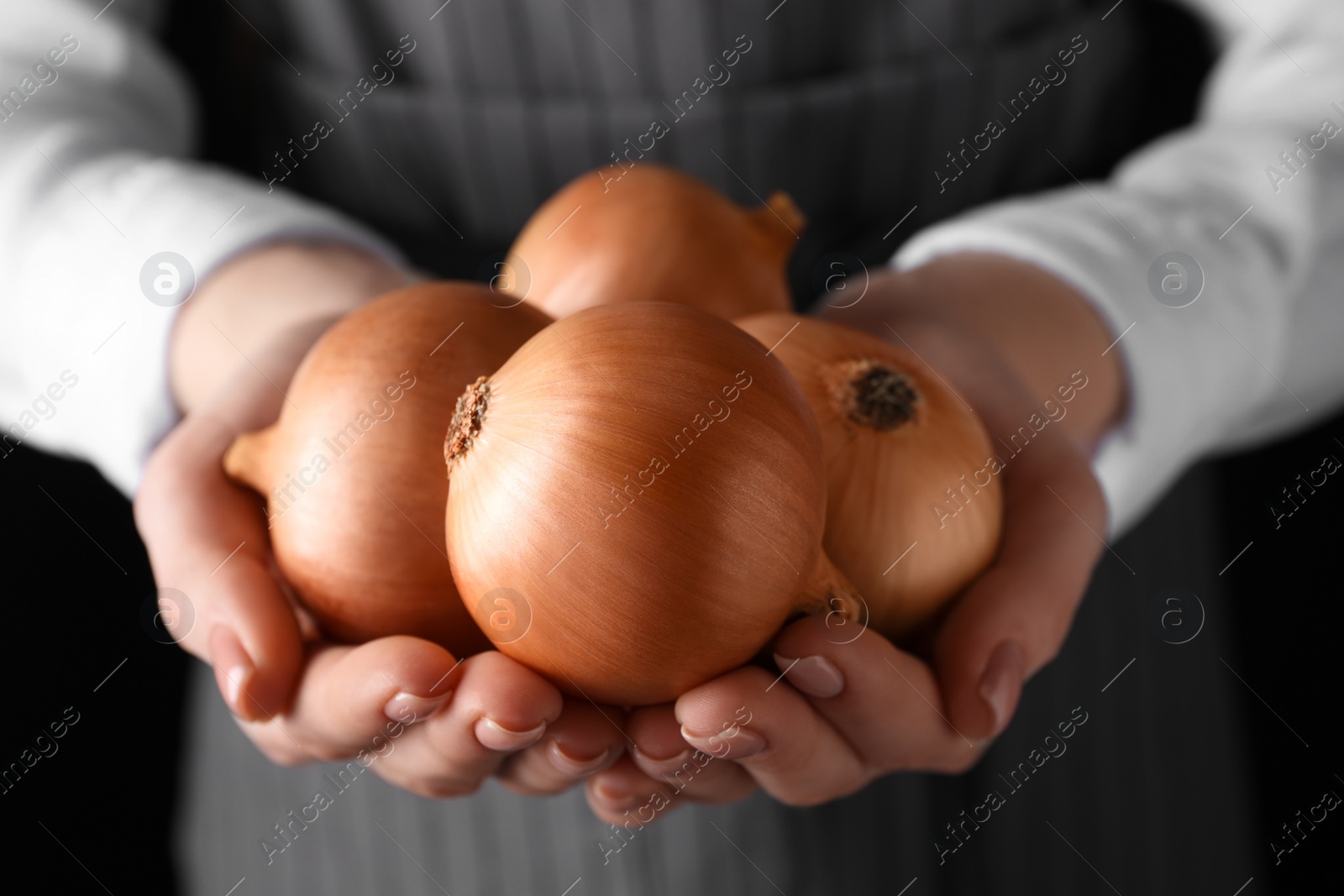 Photo of Woman holding ripe onions on black background, closeup