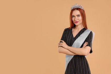 Photo of Beautiful young woman with tiara and ribbon in dress on beige background, space for text. Beauty contest